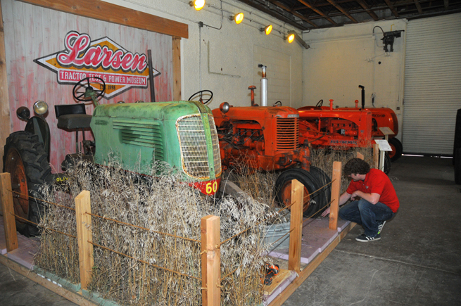 Lance Todd, manager of exhibits at the Lester F. Larsen Tractor Test and Power Museum, installs grass in a new exhibit. The project showcases an Oliver 60 and SC-Case in a setting that resembles an overgrown grass area behind a barn.